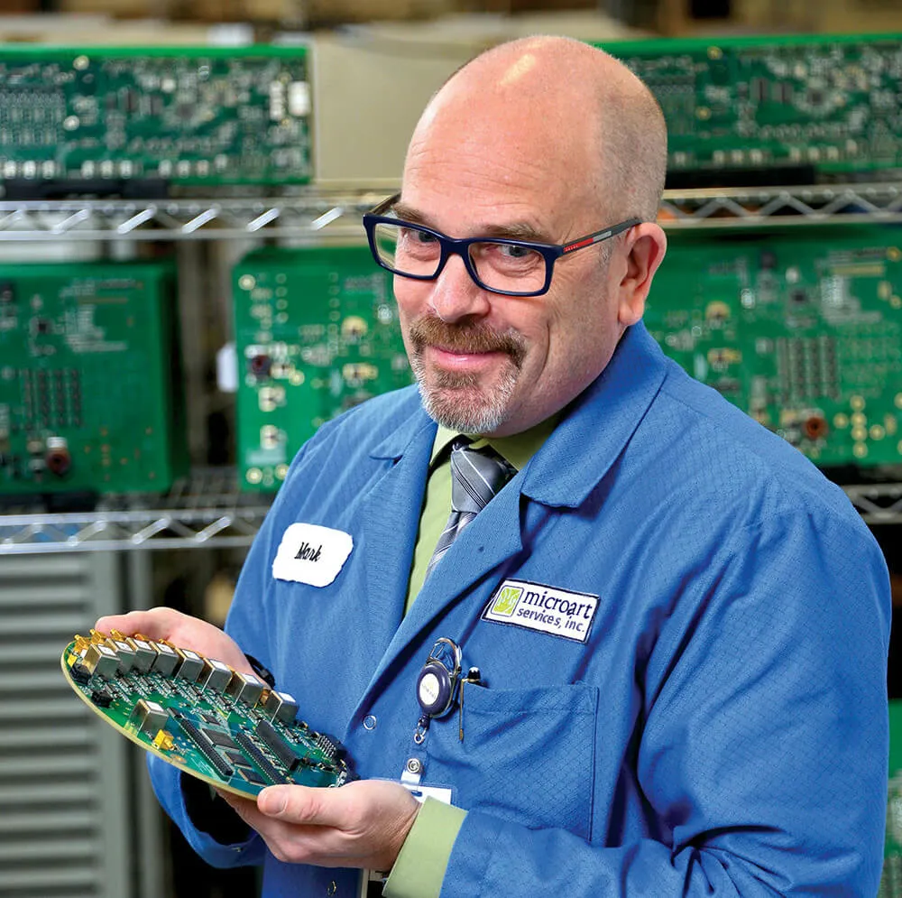 Mark Wood holding a circuit board on the Microart shop floor